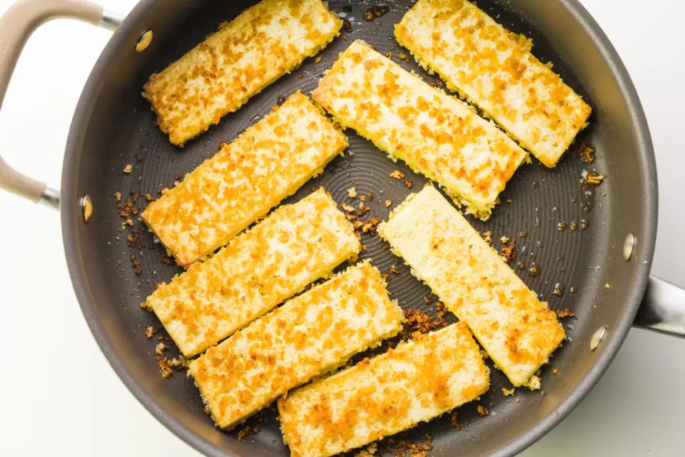 Breaded tofu is frying in a skillet and has a golden crust.