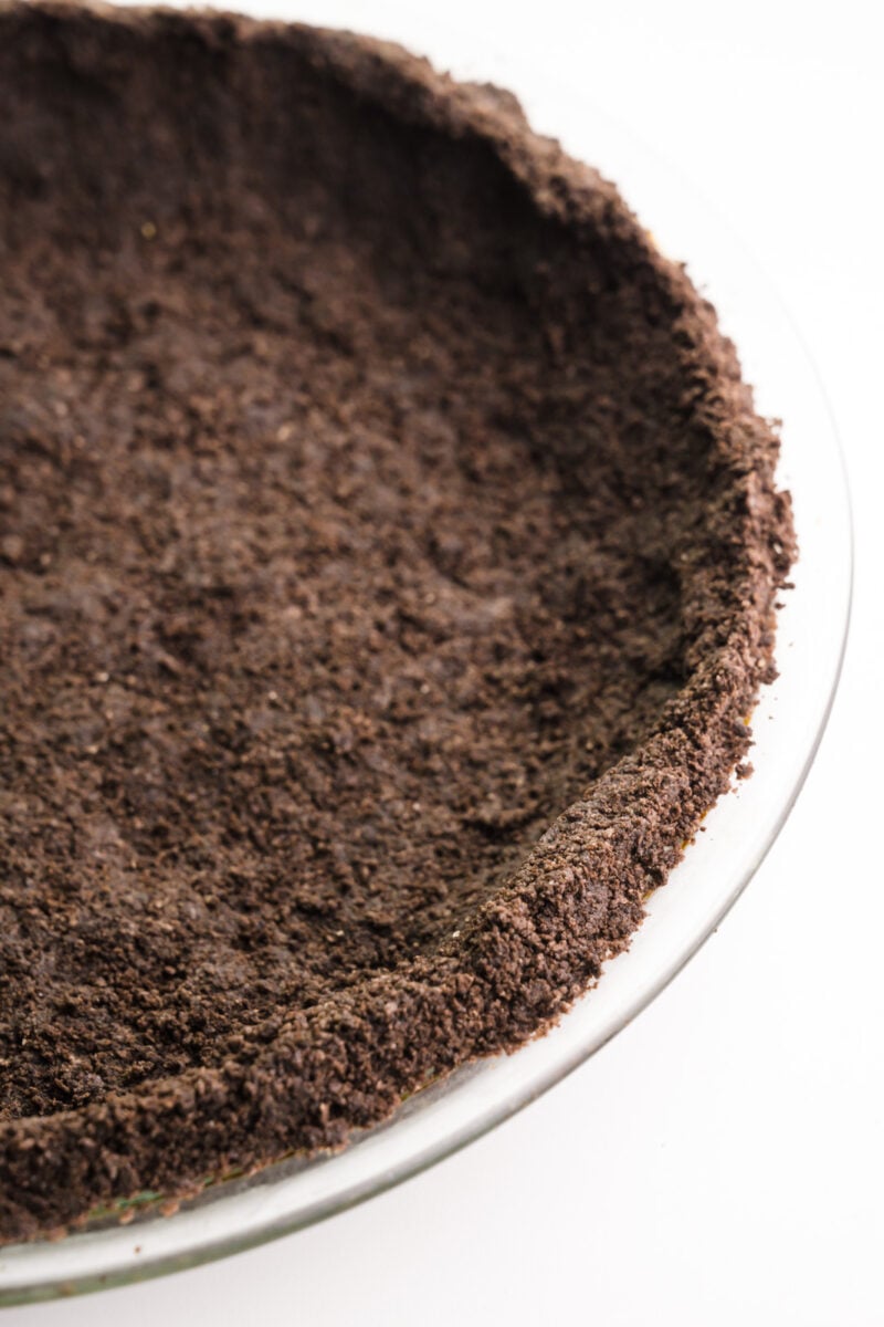 An Oreo crust has been pressed into a glass pie pan and is sitting on a white counter top.