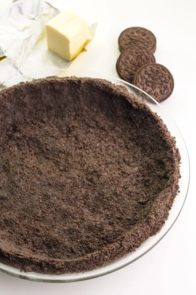 A vegan oreo pie crust sits on a counter with more sandwich cookies and a stick of vegan butter behind it.