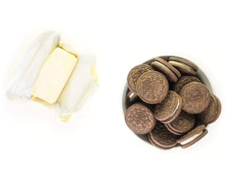 A stick of butter sits next to a bowl of chocolate sandwich cookies.