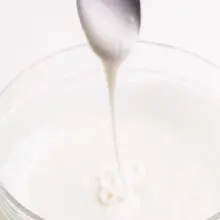 A spoon drizzles vegan royal frosting over a bowl full of more icing.