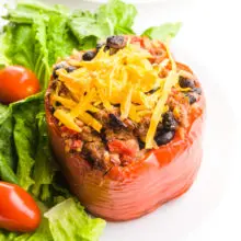 A vegan stuffed pepper has vegan cheese on top. It's sitting next to a salad with cherry tomatoes.