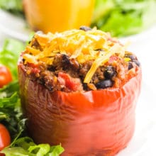 A vegan stuffed pepper sits on a white plate with a salad beside it. Another one is on a plate behind it.