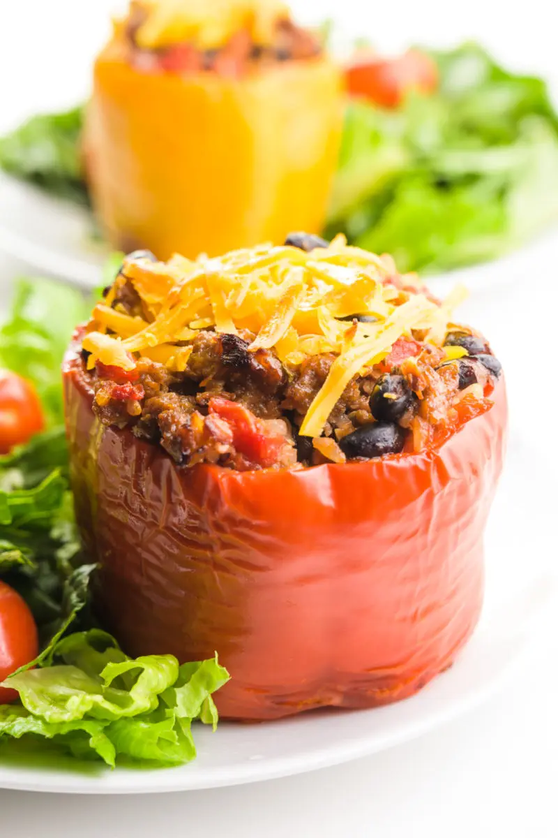 A vegan stuffed pepper sits on a white plate with a salad beside it. Another one is on a plate behind it.