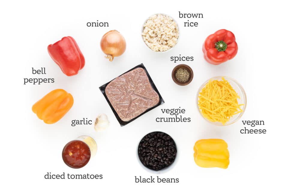 Ingredients are assembled on a white counter. The labels next to them read, "bell peppers, onion, brown rice, spices, vegan cheese, black beans, diced tomatoes, garlic, and veggie crumbles."