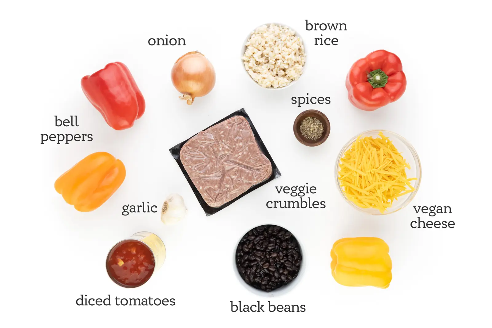 Ingredients are assembled on a white counter. The labels next to them read, "bell peppers, onion, brown rice, spices, vegan cheese, black beans, diced tomatoes, garlic, and veggie crumbles."