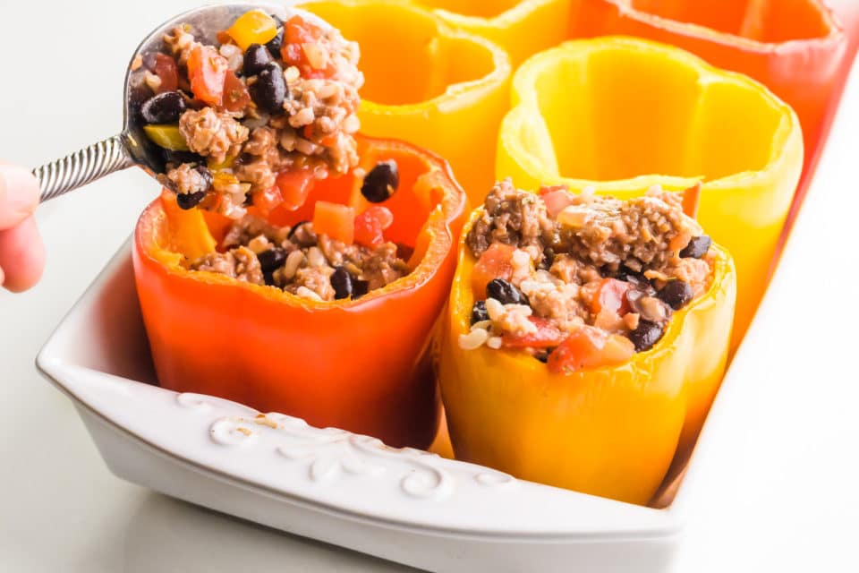 Filling is being spooned into colorful bell peppers in a baking pan.