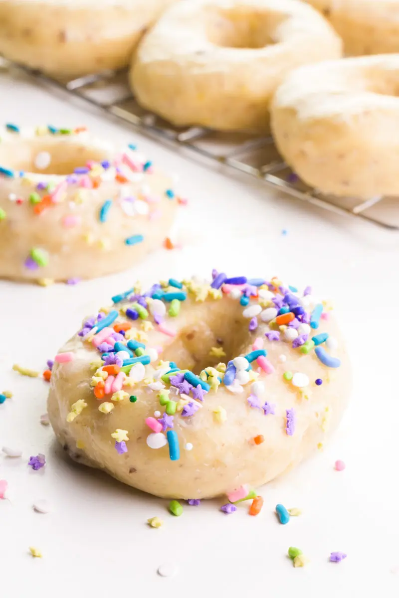 An air fryer donut has glaze and sprinkles on top. There are more glazed donuts in the background.