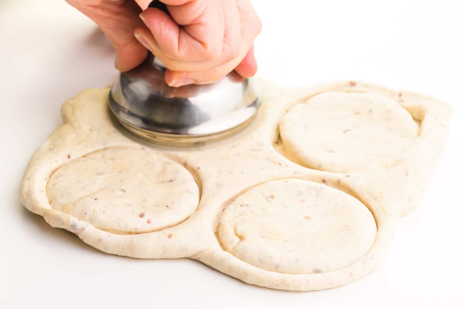 A hand holds a metal object cutting 3-inch rounds in dough.