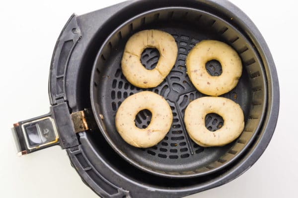 Donuts are in an air fryer basket getting ready to be fried.