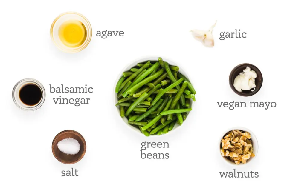 Ingredients are lined up in bowls. The labels read, "green beans, garlic, vegan mayo, walnuts, salt, balsamic vinegar, and agave."