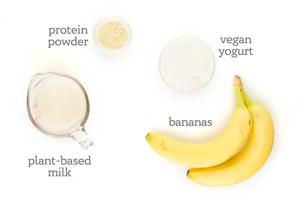 Ingredients are on a white counter. The labels read, "bananas, plant-based milk, protein powder, and vegan yogurt."
