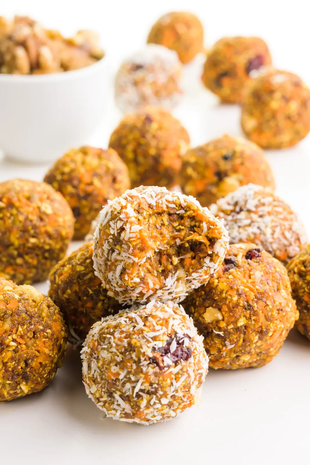 A group of carrot cake energy balls sits around a bowl of walnuts. One of the treats has a bite taken out of it.