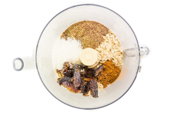 Looking down on a food processor bowl full of oats, ground flax, coconut flakes, dates, and spices.