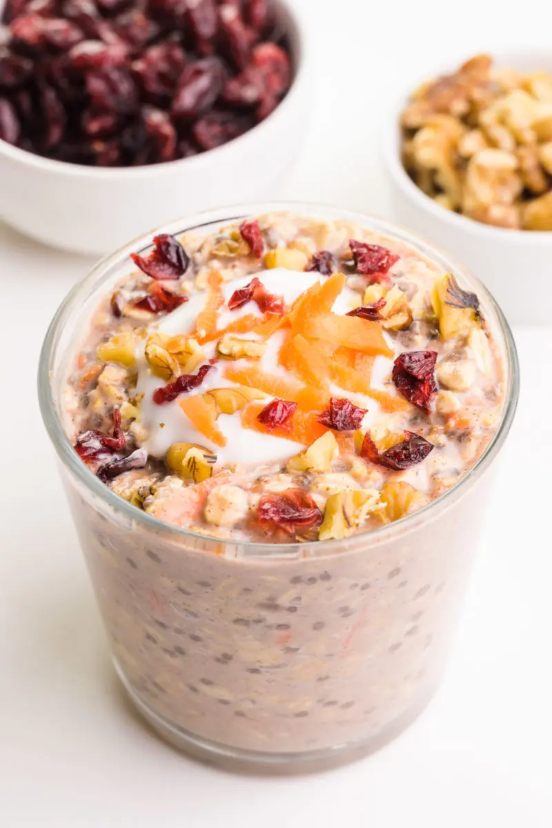 Looking down on a glass with overnight oats. There's a bowl of dried cranberries and walnuts.