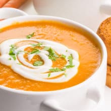 A close-up of a bowl of carrot ginger soup with cream and chopped parsley on top.