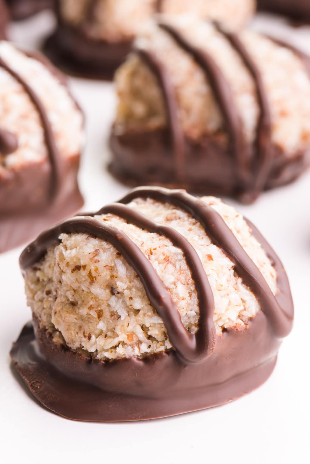 A chocolate coconut macaroon cookie has chocolate drizzles over the top and sits in front of more of the cookies.