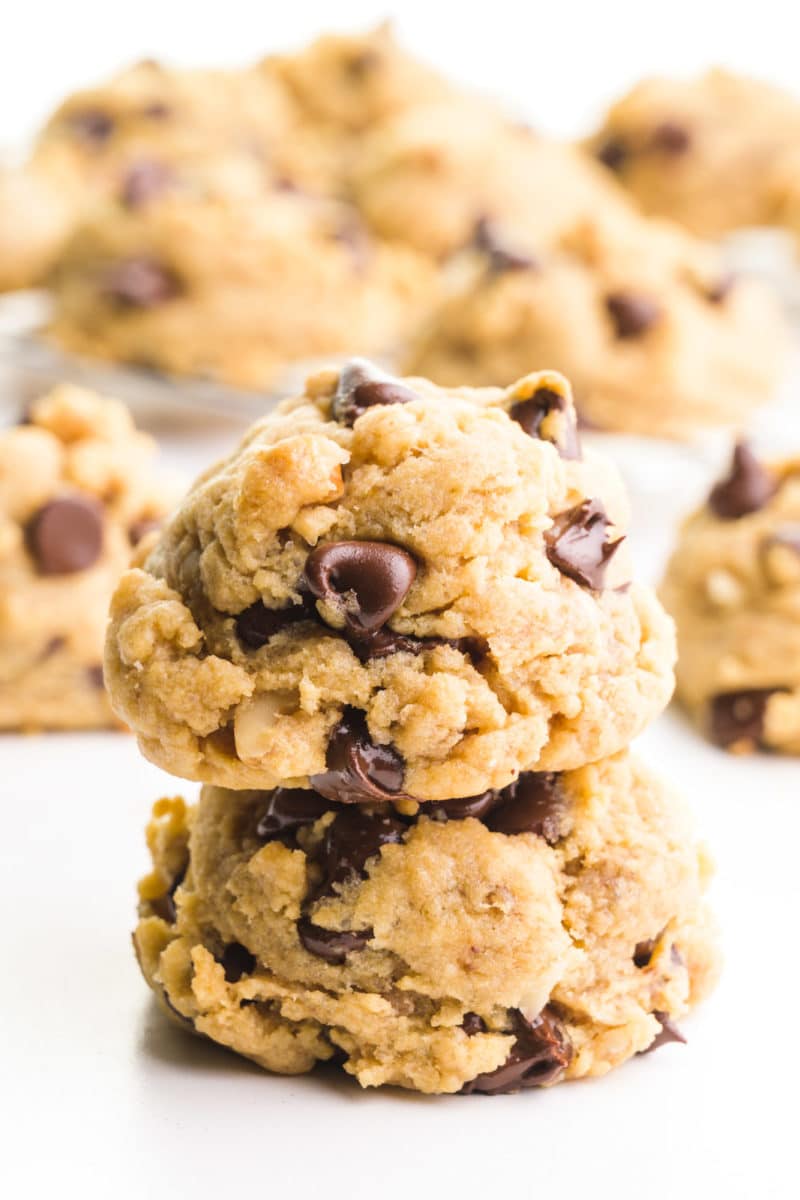 A stack of banana cookies with chocolate chips is in the foreground. There are more cookies in the background.