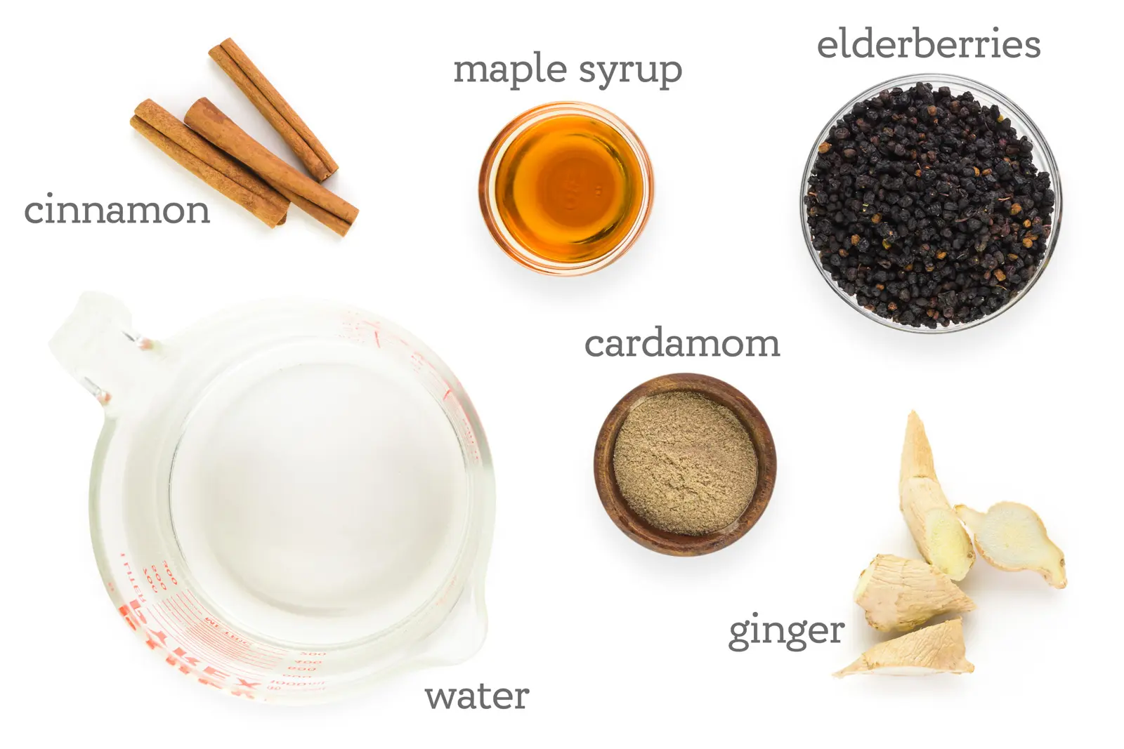 Ingredients are on a table. The labels read, "Cinnamon, maple syrup, elderberries, cardamom, ginger, and water."