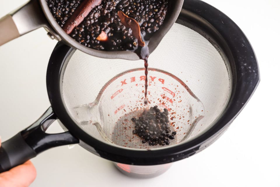 A pan is pouring syrup into a strainer into a smaller bowl.