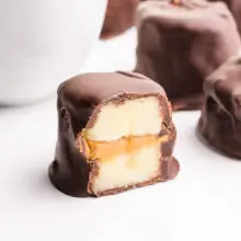 A frozen banana bite is cut in half, reveling banana slices with peanut butter in the middle. It's all coated in chocolate. There are more of the treats in the background.