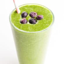 A green smoothie has blueberries on top and a pink straw on the side.