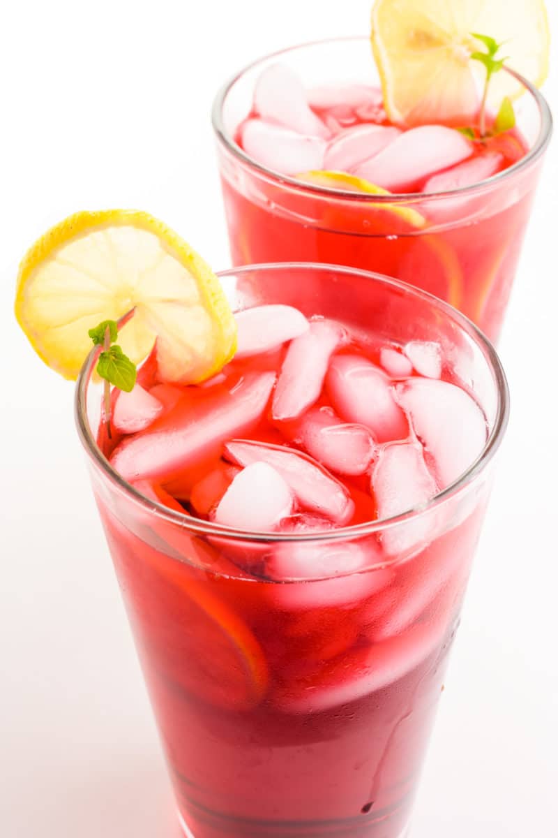 Two glasses of hibiscus tea have lemon slices on the side and ice in the glasses.