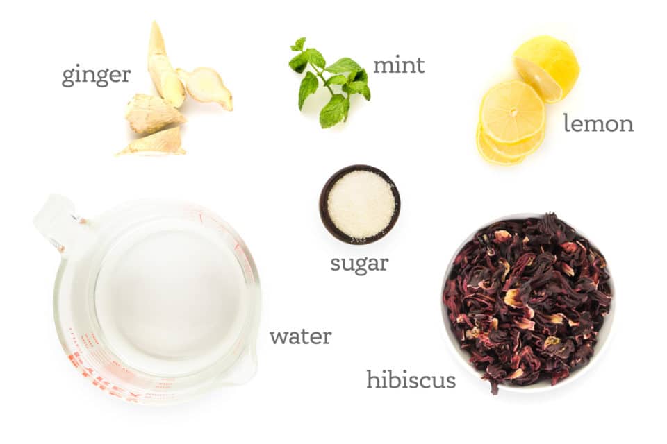 Ingredients are on a white counter. The labels read, "Hibiscus, sugar, water, ginger, mint, and lemon."