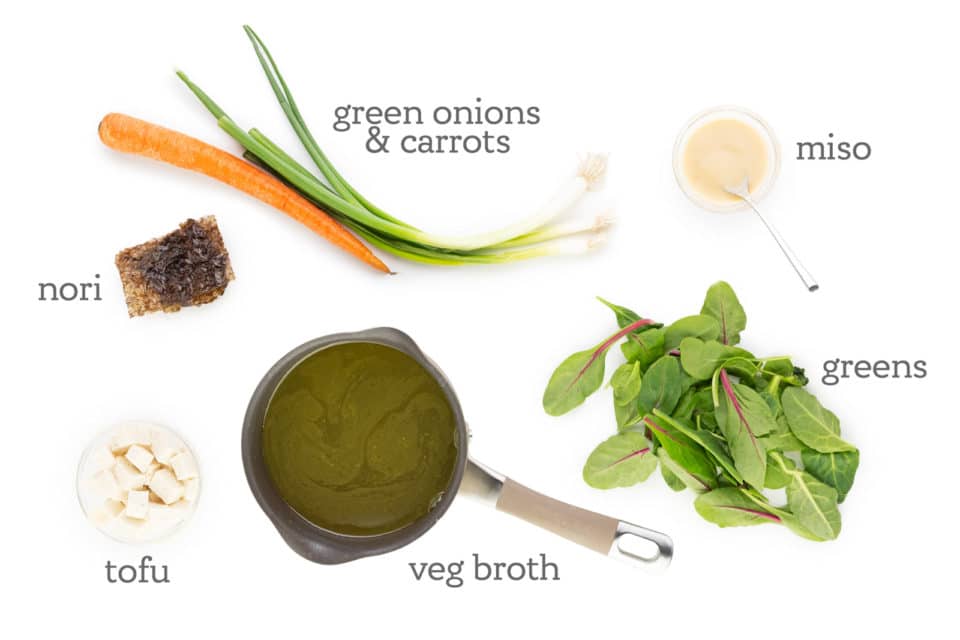 Ingredients are placed on a white counter. The labels read, "Miso, greens, veg broth, tofu, nori, green onions & carrots."