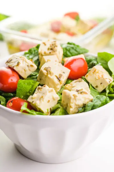 A bowl holds a salad full of greens, cherry tomatoes, and tofu feta cubes.