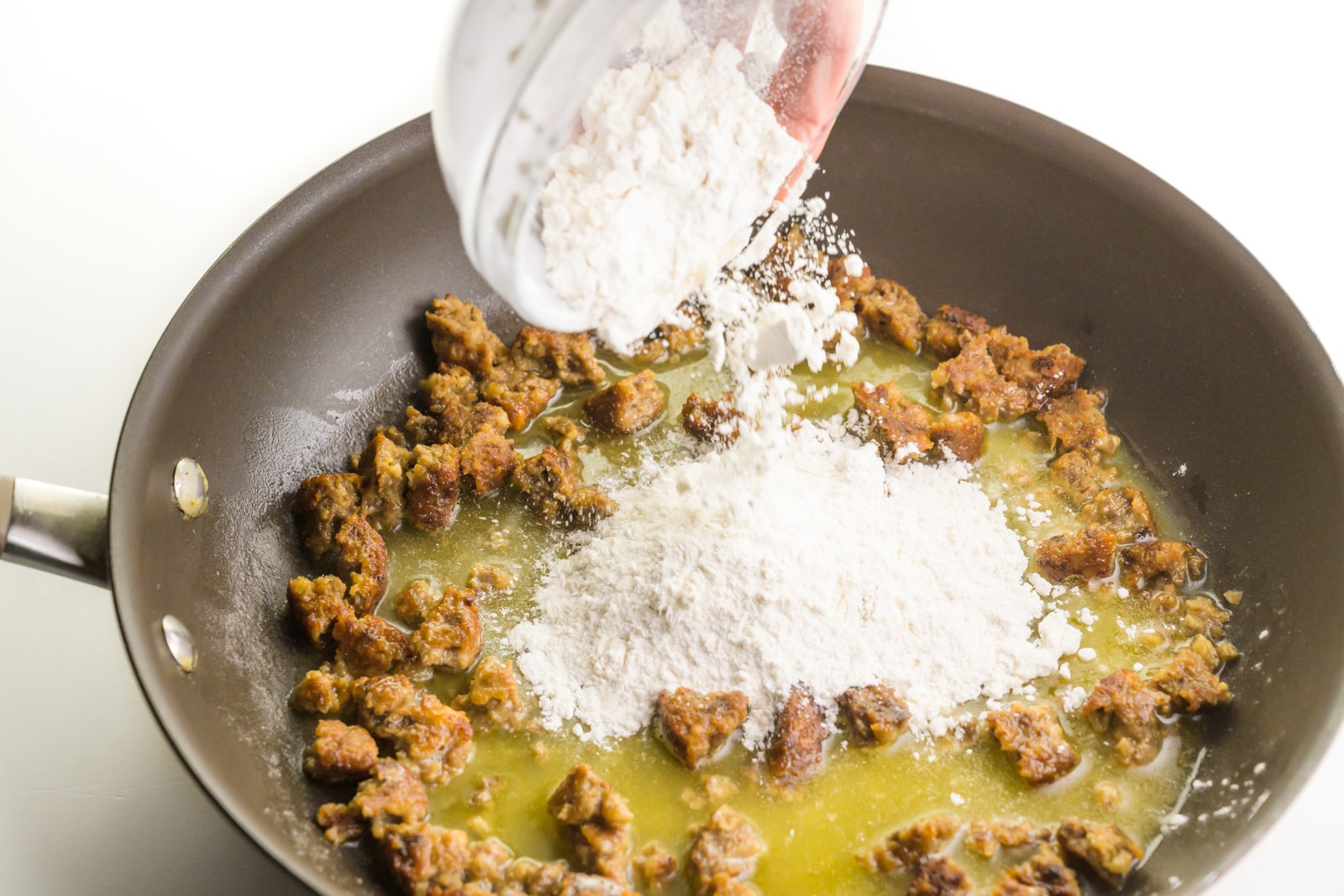 Flour is being poured into a skillet with other ingredients.