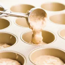 A cookie scooper is distributing batter into a muffin tin.
