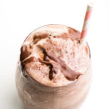 Looking down on a chocolate milkshake in a glass with chocolate syrup on top and a straw.