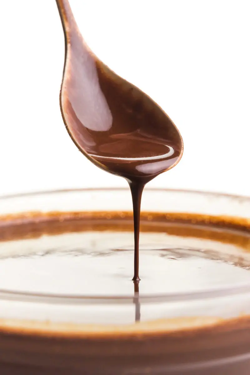 A close-up of a spoon of chocolate sauce drizzling it into a bowl with more of it.
