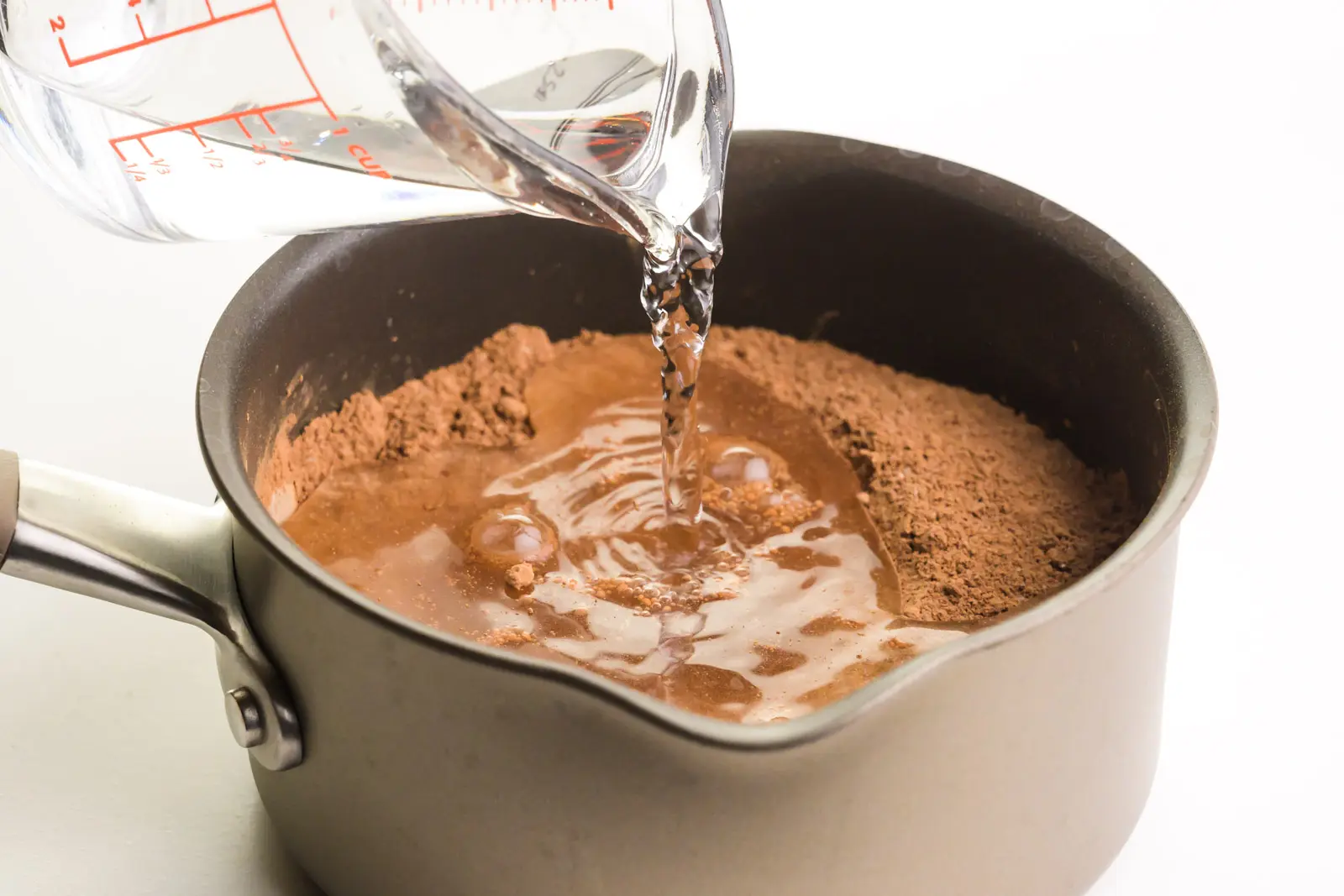 Water is being poured into a saucepan with cocoa powder.