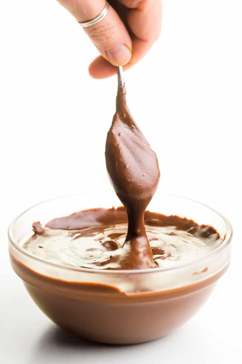 A spoon full of melted chocolate hovers over a bowl with more of the chocolate mixture.
