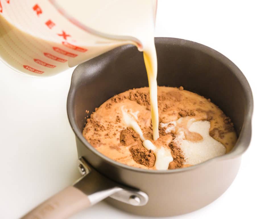 Milk is being poured into a saucepan with cocoa powder.