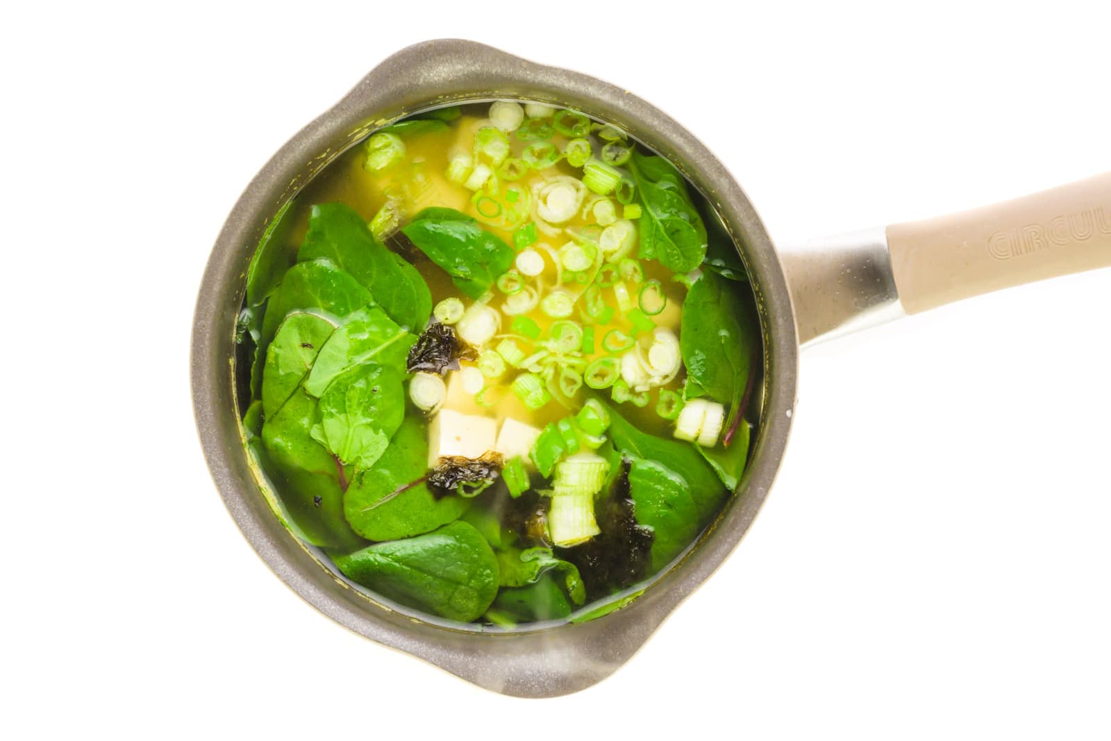 Looking down on a saucepan with greens, tofu, and cut green onions.