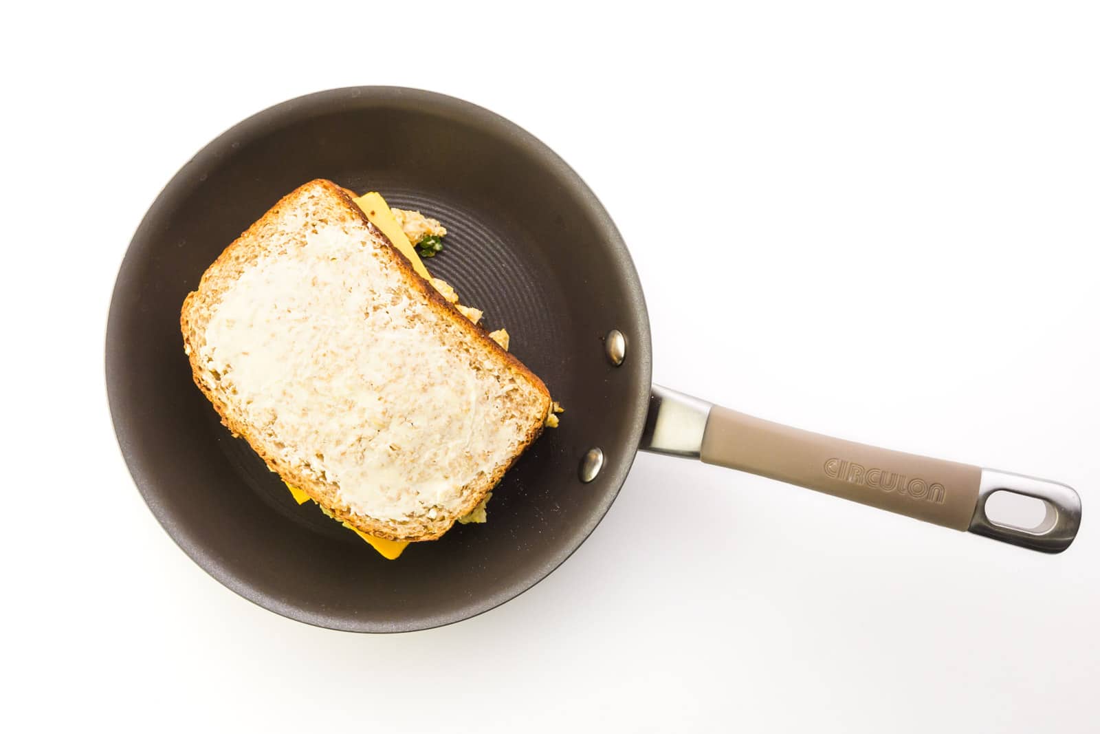 A skillet holds a sandwich with buttered bread on top.