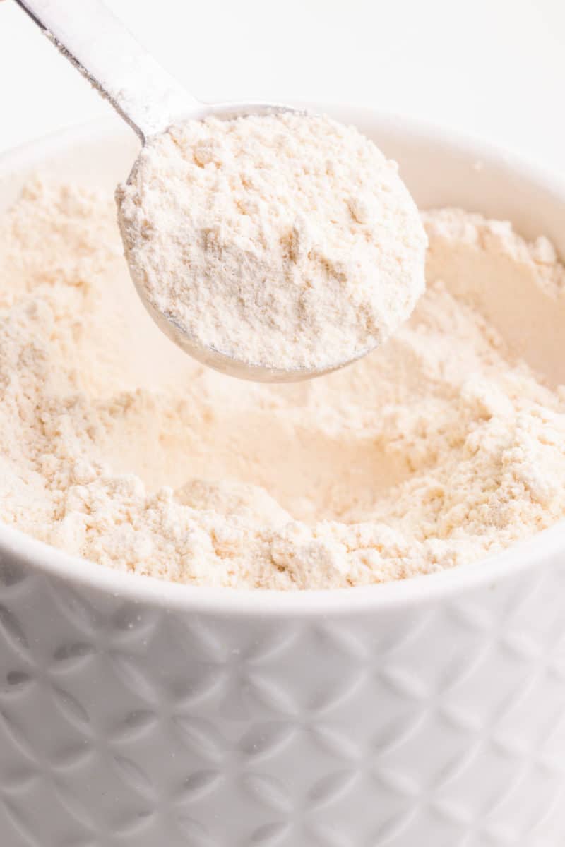 A measuring spoon full of whole wheat pastry flour hovers over a bowl with more of it.