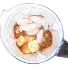 Looking down on a blender jar with ice cubes, banana chunks, and chocolate protein powder,
