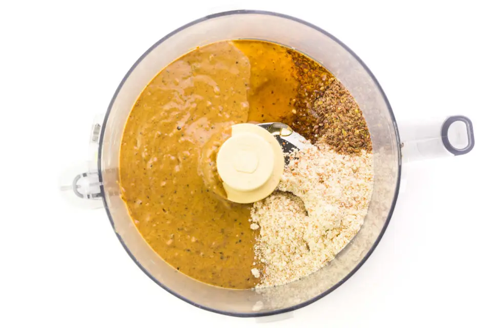 Ingredients are in the bottom of a food processor including almond butter, ground flax seed, almond flour and more.