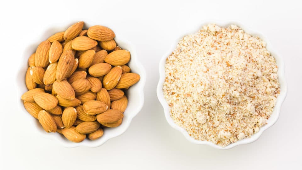 Two bowls hold almonds with the skins on and almond meal.