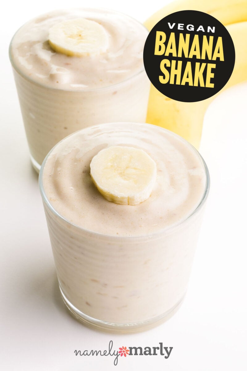 A banana milkshake is in a glass with a slice of banana on top. There's a second glass and some bananas in the background and text that reads vegan banana shake