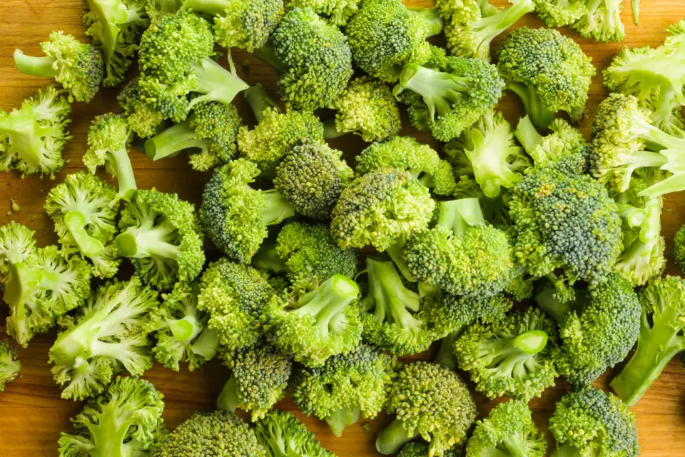 Several broccoli florets are grouped together on a wooden cutting board.