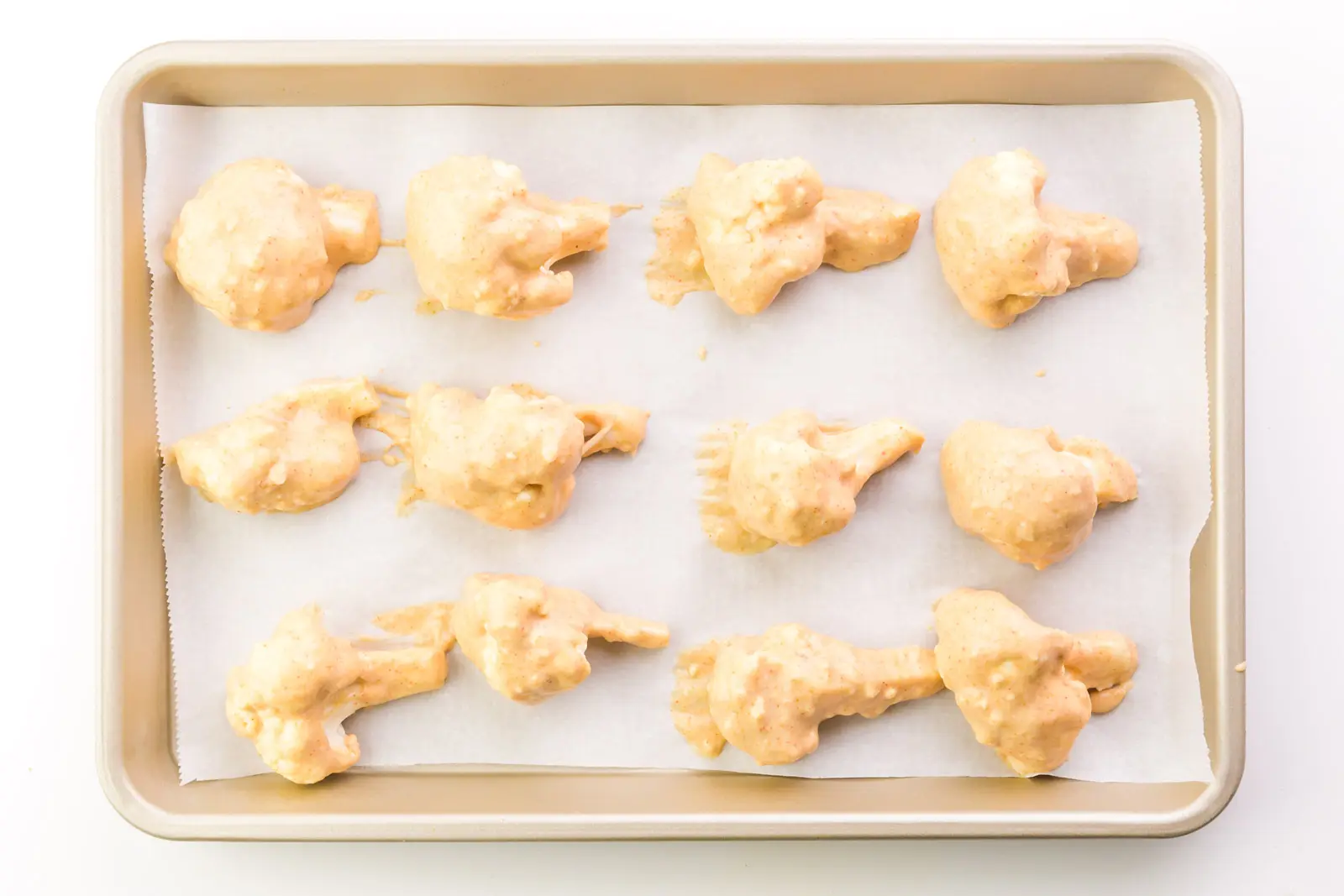 Cauliflower florets have been dipped in batter and baked until crispy. They're laid out in rows on a baking sheet lined with parchment paper.