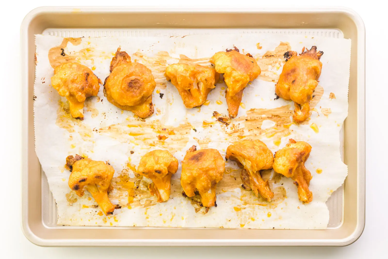 Cauliflower wings are lined up on a baking sheet lined with parchment paper. They're golden brown in spots.