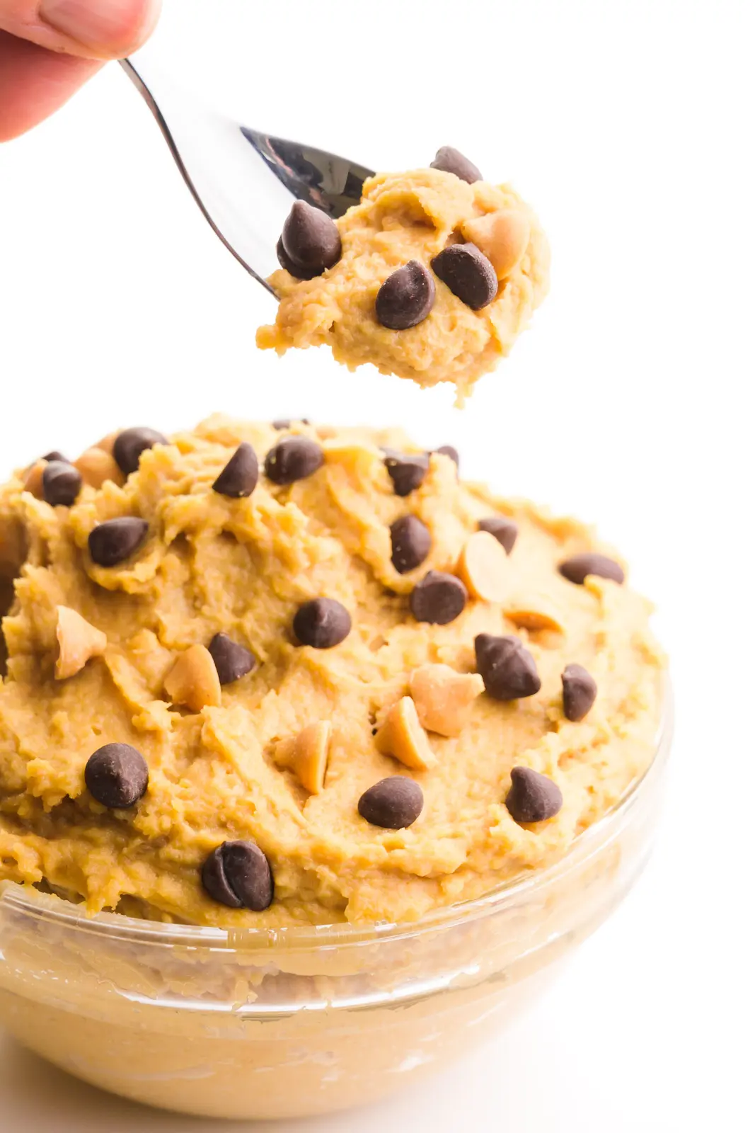 A hand holds a spoonful of cookie dough hovering over a bowl full of more cookie dough.