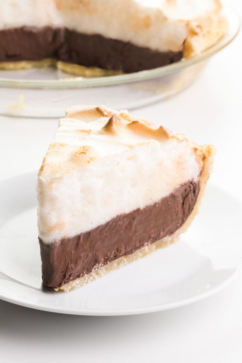 A slice of chocolate meringue pie sits on a plate. The rest of the pie is behind it.