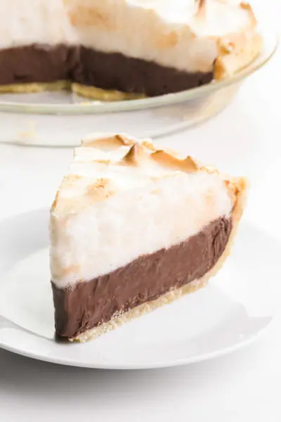 A slice of chocolate meringue pie sits on a plate. The rest of the pie is behind it.